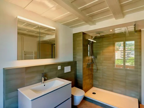 Badezimmer mit hellgrünen Wandfliesen und Glasduschwand.