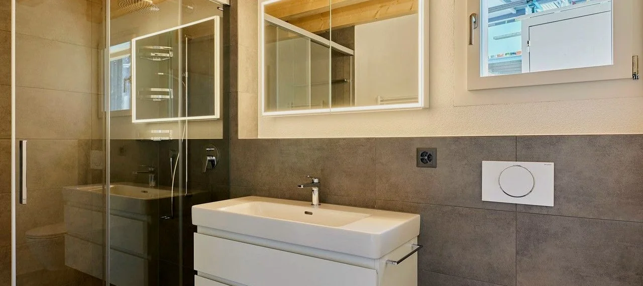 Badezimmer mit Waschtisch, Glasdusche und Holzbalkendecke.