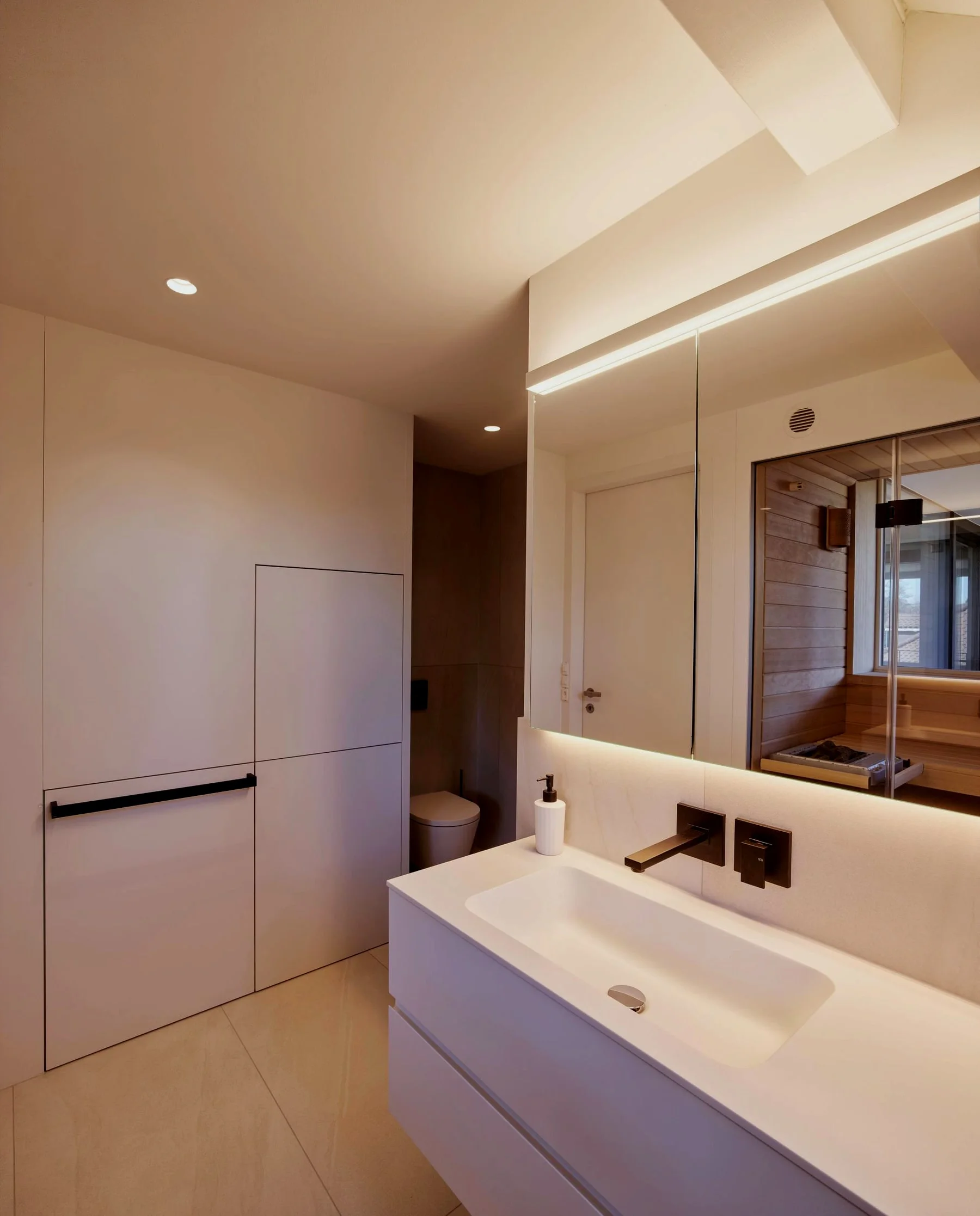 Modernes Badezimmer mit Waschtisch, Wandarmaturen und beleuchtetem Spiegel.