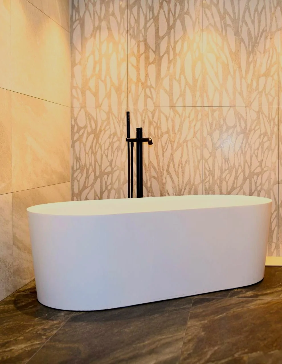 Freistehende Badewanne mit Standarmatur vor Fliesenwand.